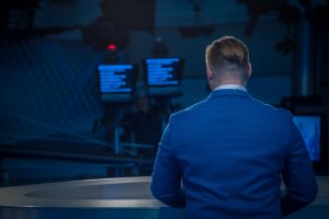 123rf - Aleksandr Fedorov Homem vestindo terno, de costas para a foto, lendo um teleprompter dentro de um estúdio.