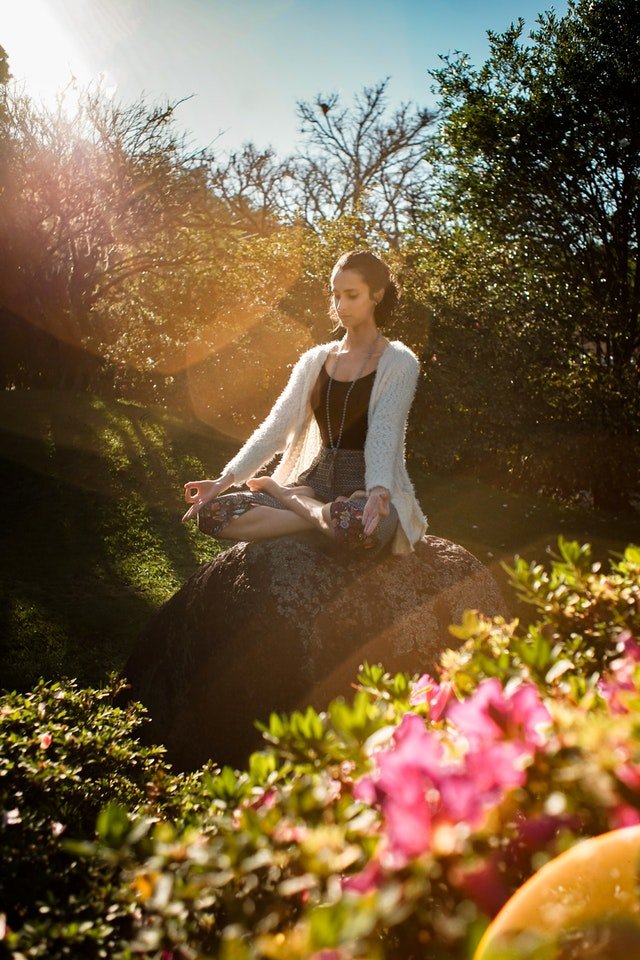 Garota sentada em pedra meditando em posição de lótus
