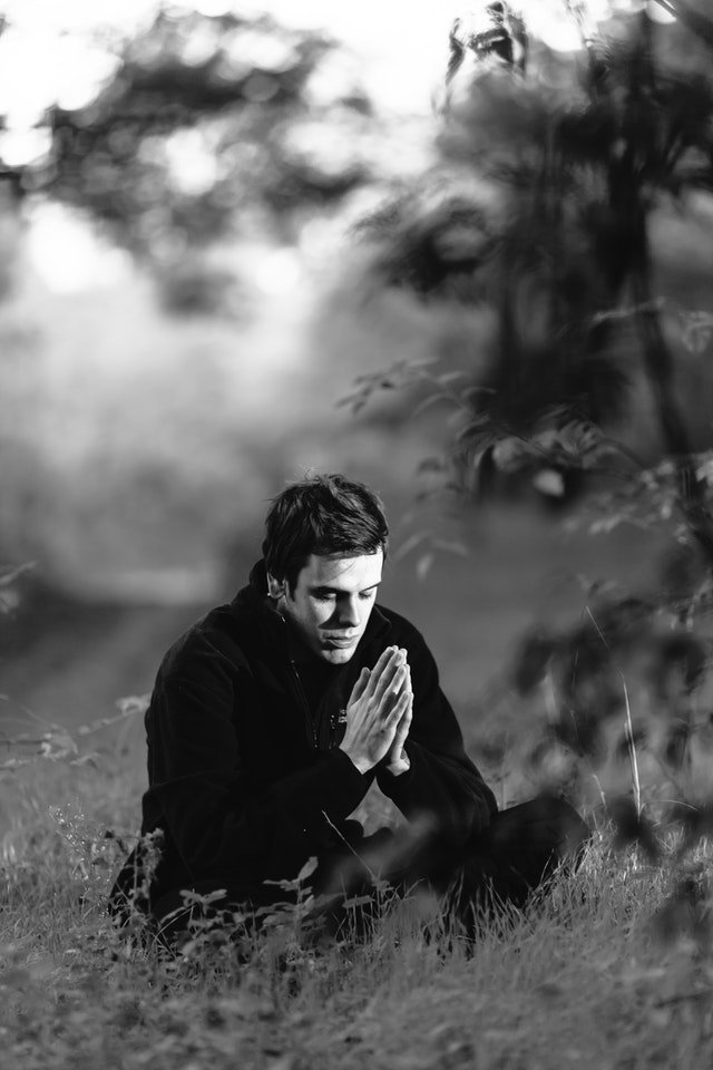Homem sentado na grama rezando em preto e branco