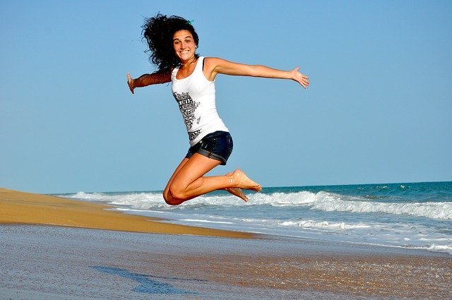 Mulher pulando e sorrindo em praia com mar ao fundo