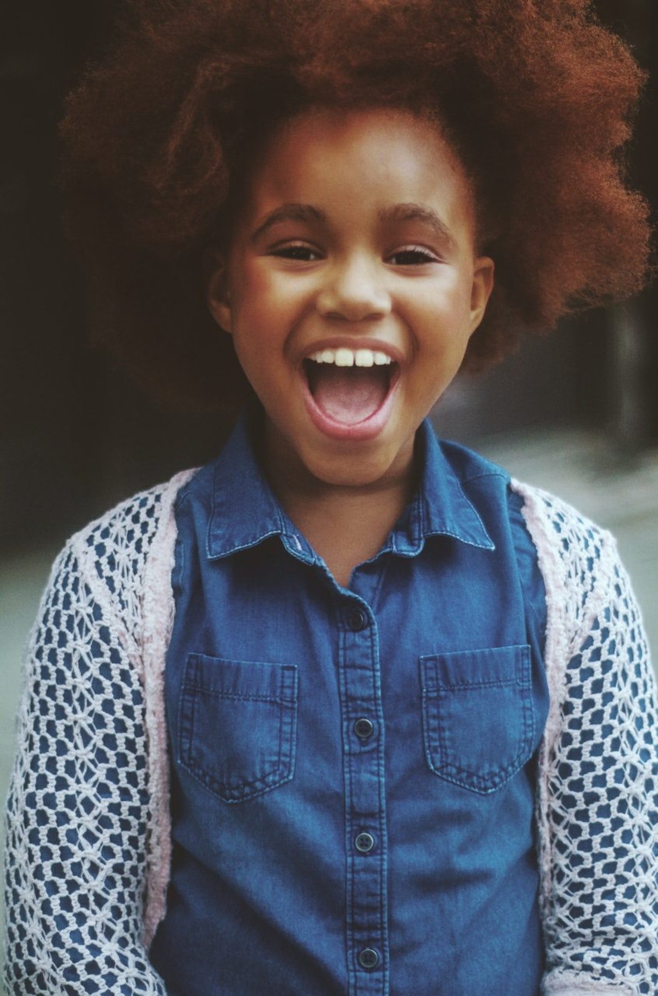 Criança de cabelo afro usando uma camiseta jeans e sorrindo.