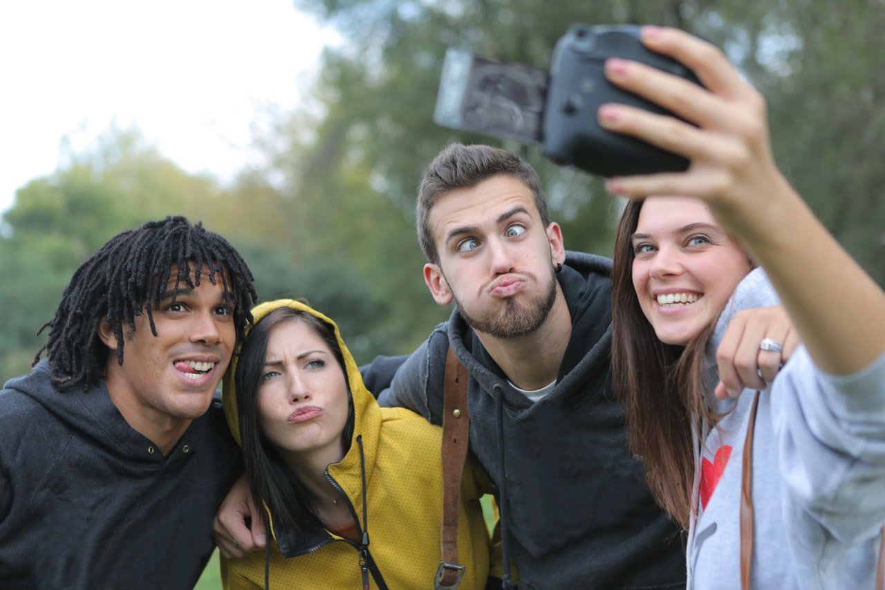 Grupo de quatro amigos rindo e fazendo caretas enquanto tiram selfie.