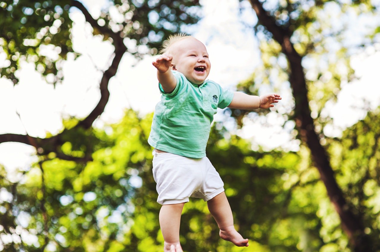 Bebê rindo enquanto é jogado para cima, em um parque natural.