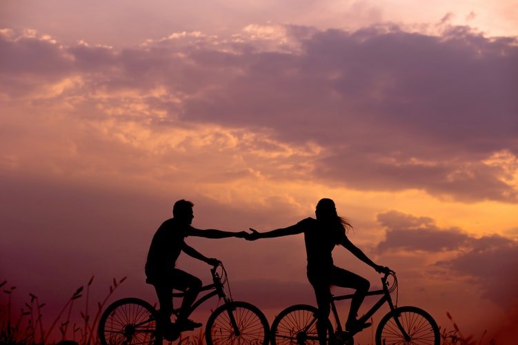 Silhueta de casal andando de bicicleta de mãos dadas