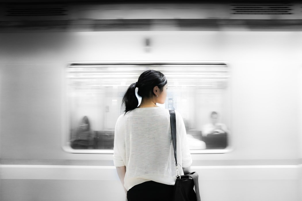 Mulher olhando para o lado enquanto um metrô passa à frente.