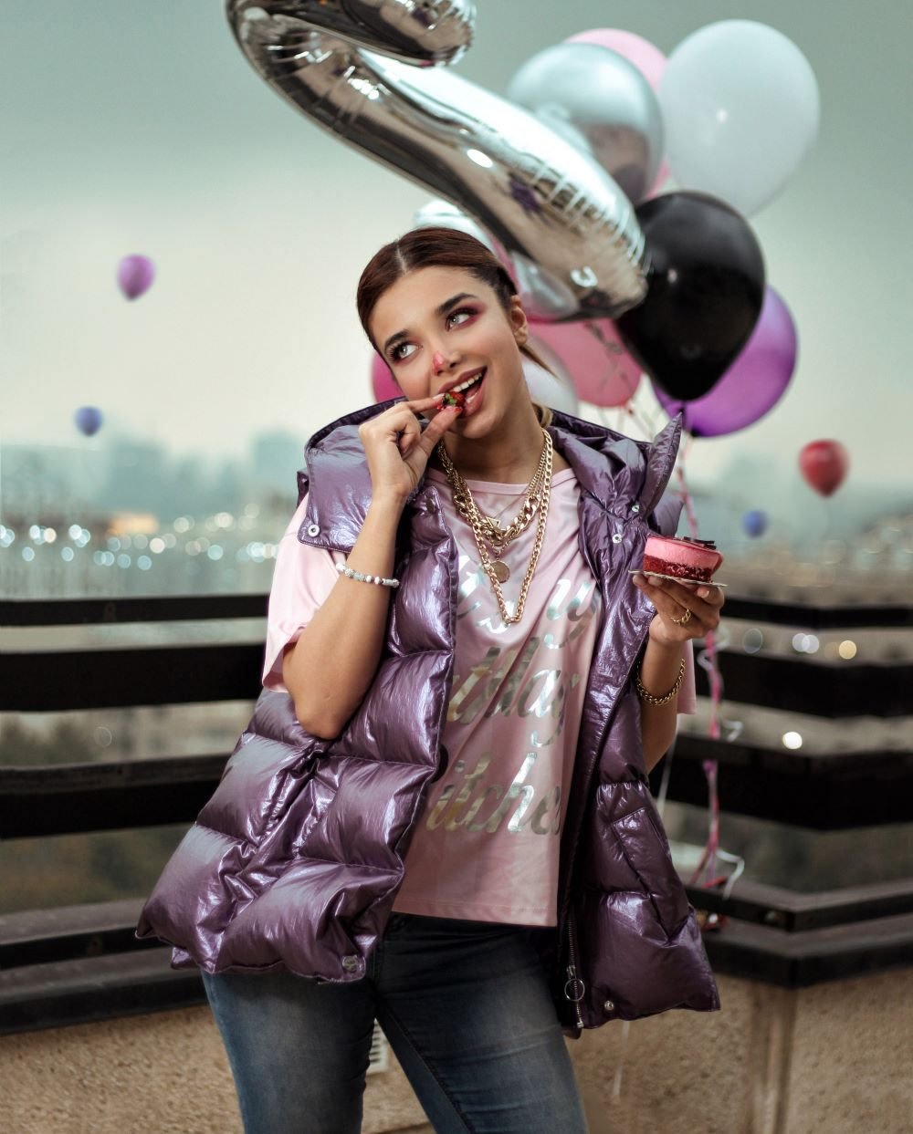 Garota segurando balões de festa comendo um doce.