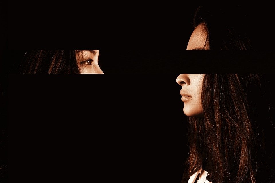 Mulher de perfil, com uma faixa na altura dos olhos recortada da foto. A faixa recortada está de frente para a mulher, do outro lado da imagem, onde o fundo é todo preto.