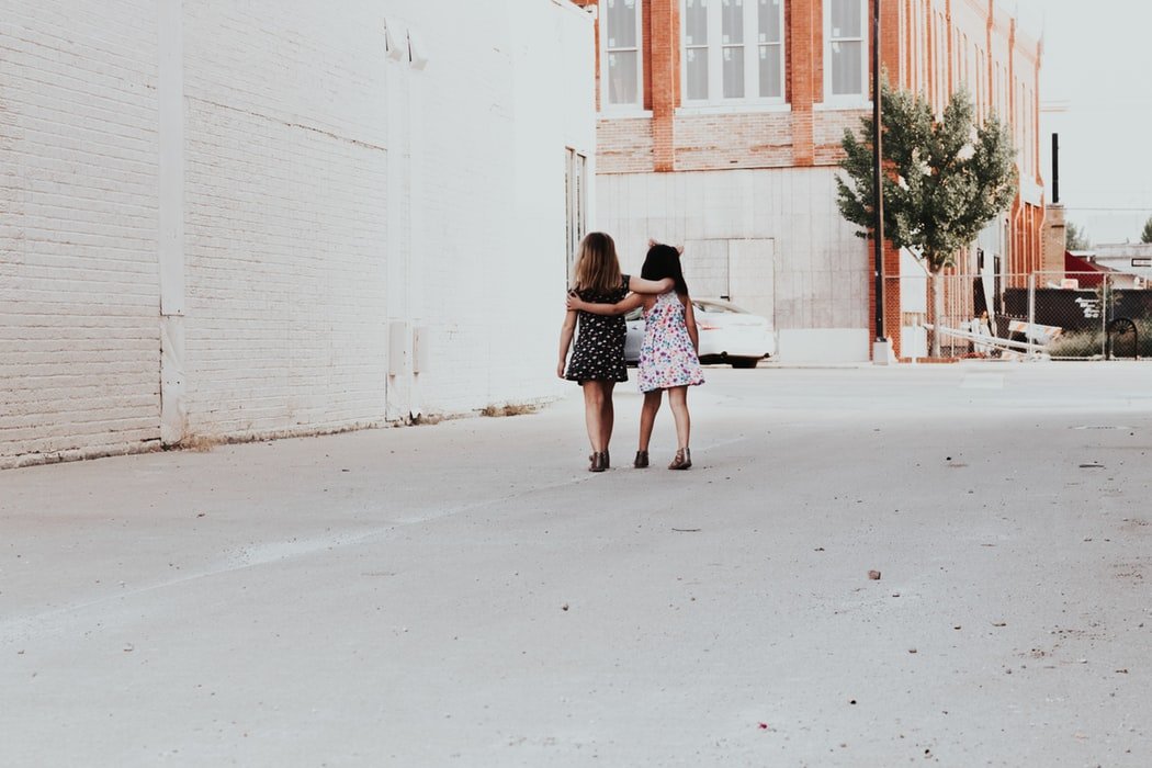 Duas meninas pequenas andando juntas enquanto se abraçam.