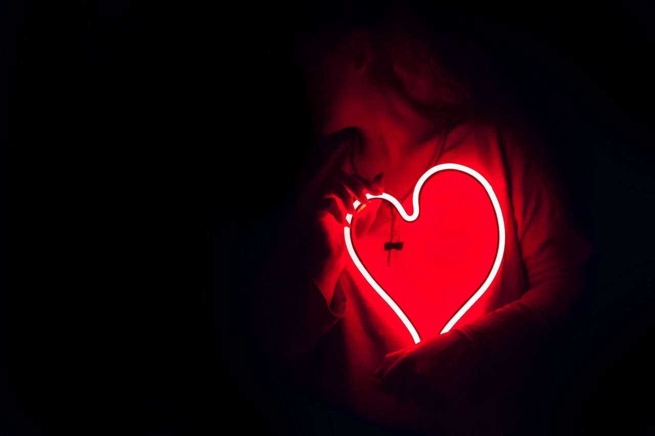 Mulher segurando um coração neon sobre o peito.