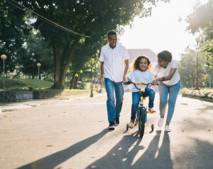 Foto de Agung Pandit Wiguna no Pexels Casal ensinando a filha a andar de bicicleta.