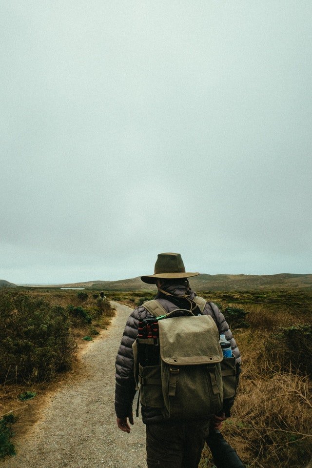 Homem de costas com mochila e chapéu caminhando em trilha
