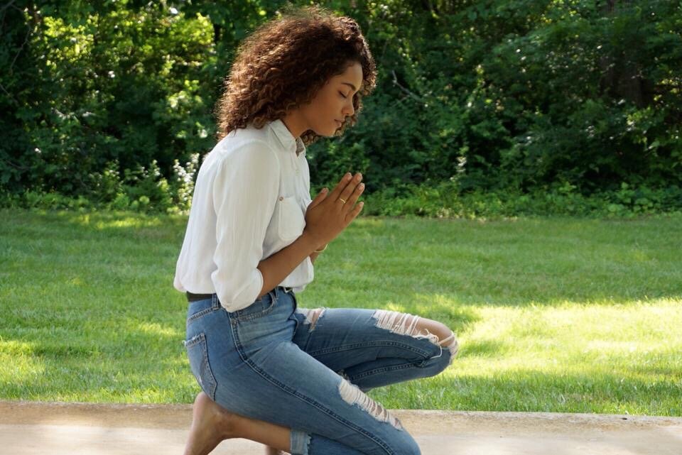 Mulher ajoelhada ao lado de um gramado rezando