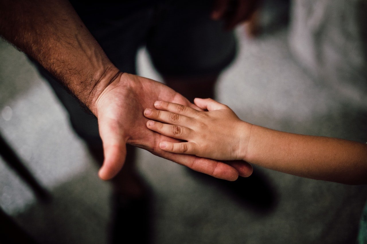 Adulto segurando a mão de uma criança.