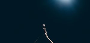Amaury Gutierrez/Unsplash Mãos rezando para o alto com um fundo escuro.