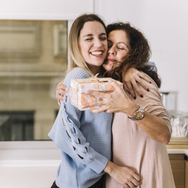 Mulher abraçando sua mãe que segura uma caixa de presente.