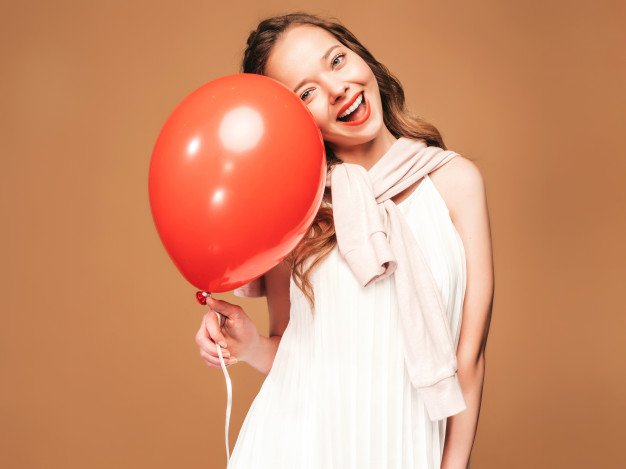 Mulher sorrindo e segurando um grande balão vermelho.