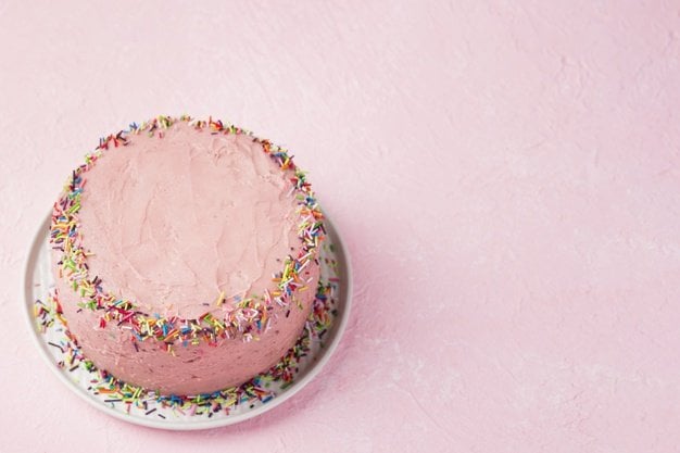Bolo de aniversário com cobertura rosa e granulados coloridos.