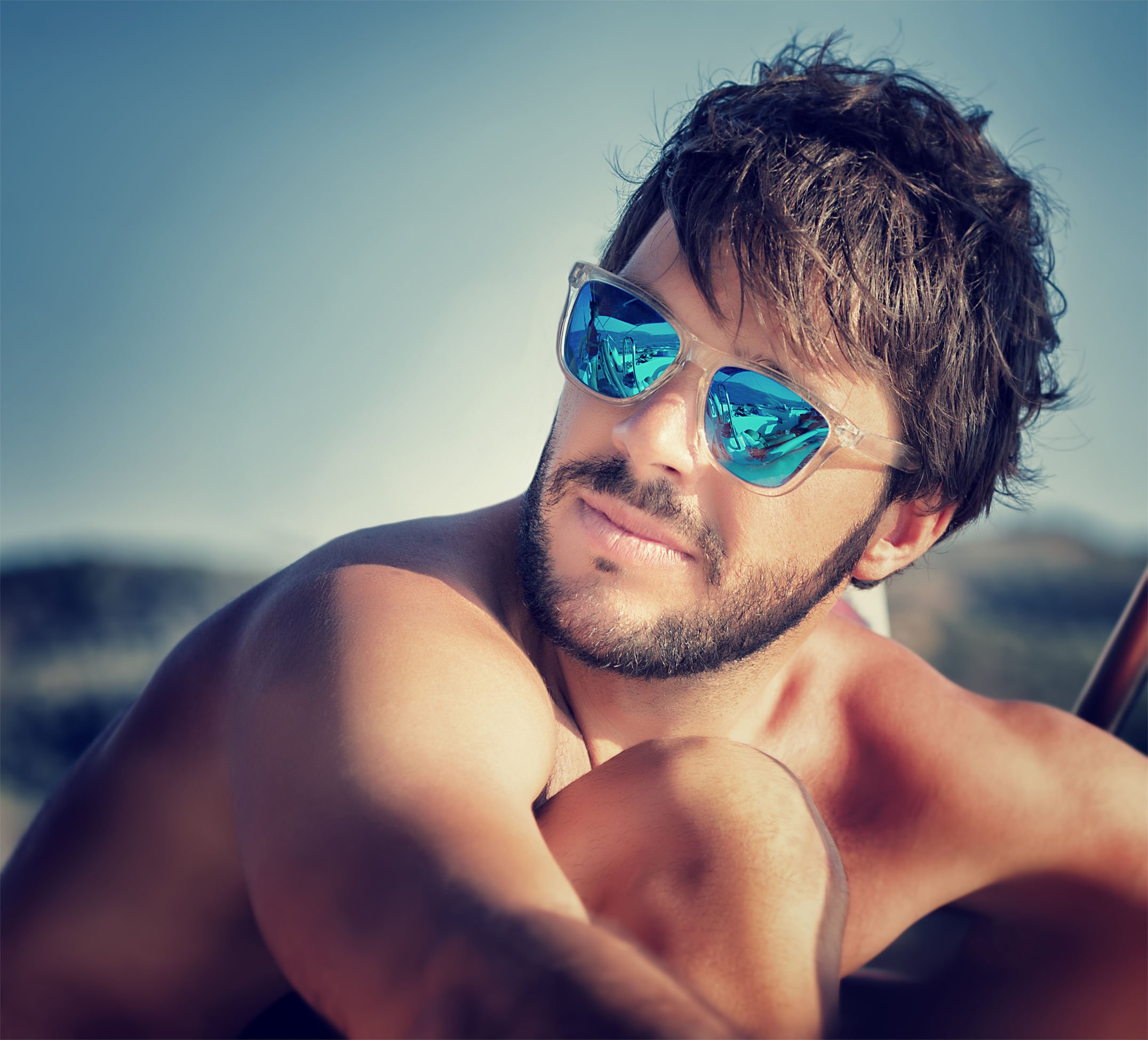 Foto de homem de óculos de sol, sentado na praia