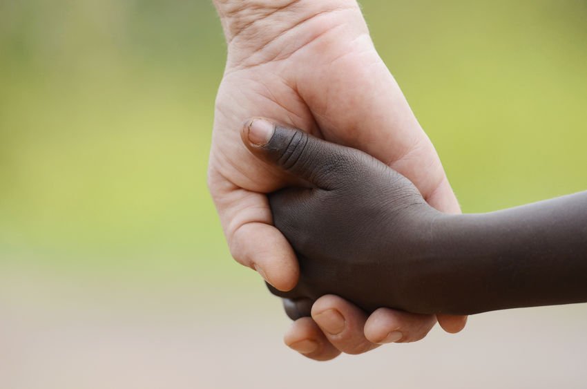 Criança negra dando a mão para pessoa branca