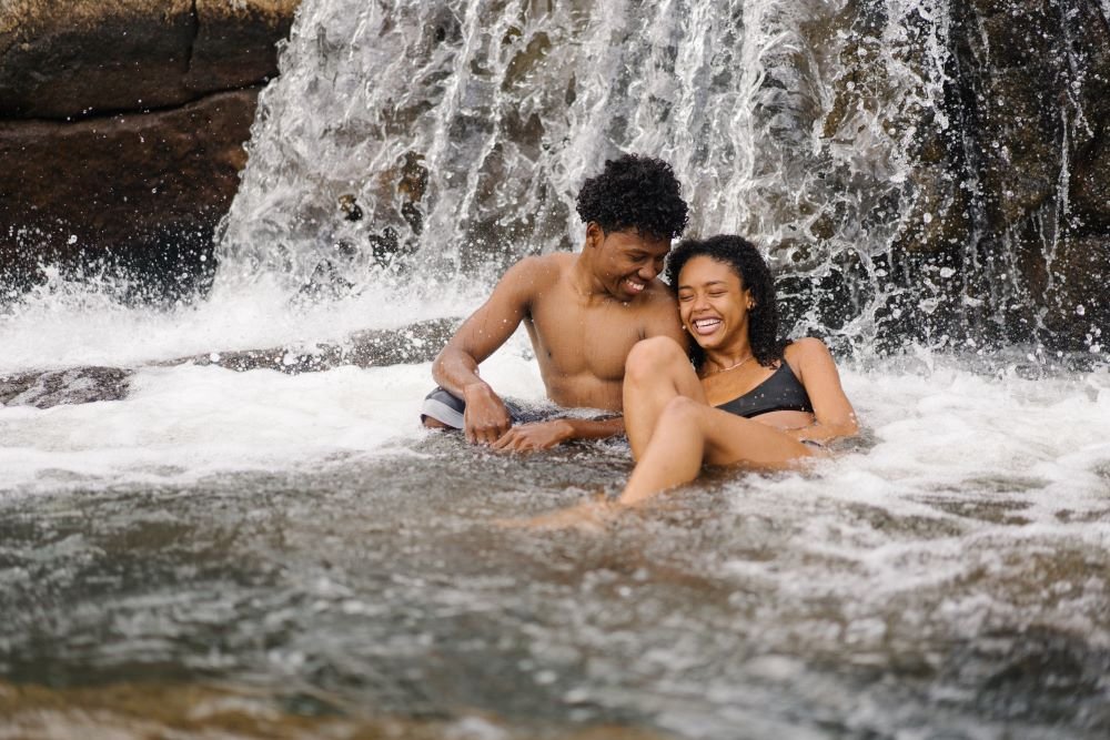 Casal sorrindo tomando banho de cachoeira.