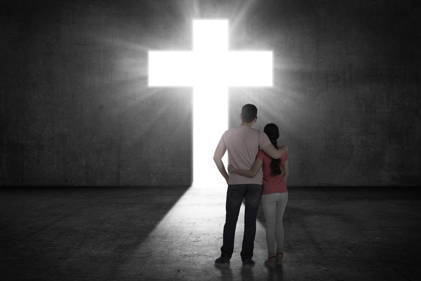 Casal abraçado em frente a cruz brilhando