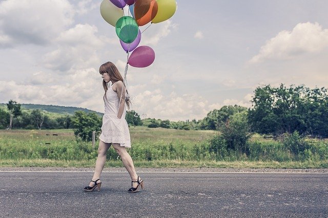 Menina caminhando em estrada com balões de aniversário