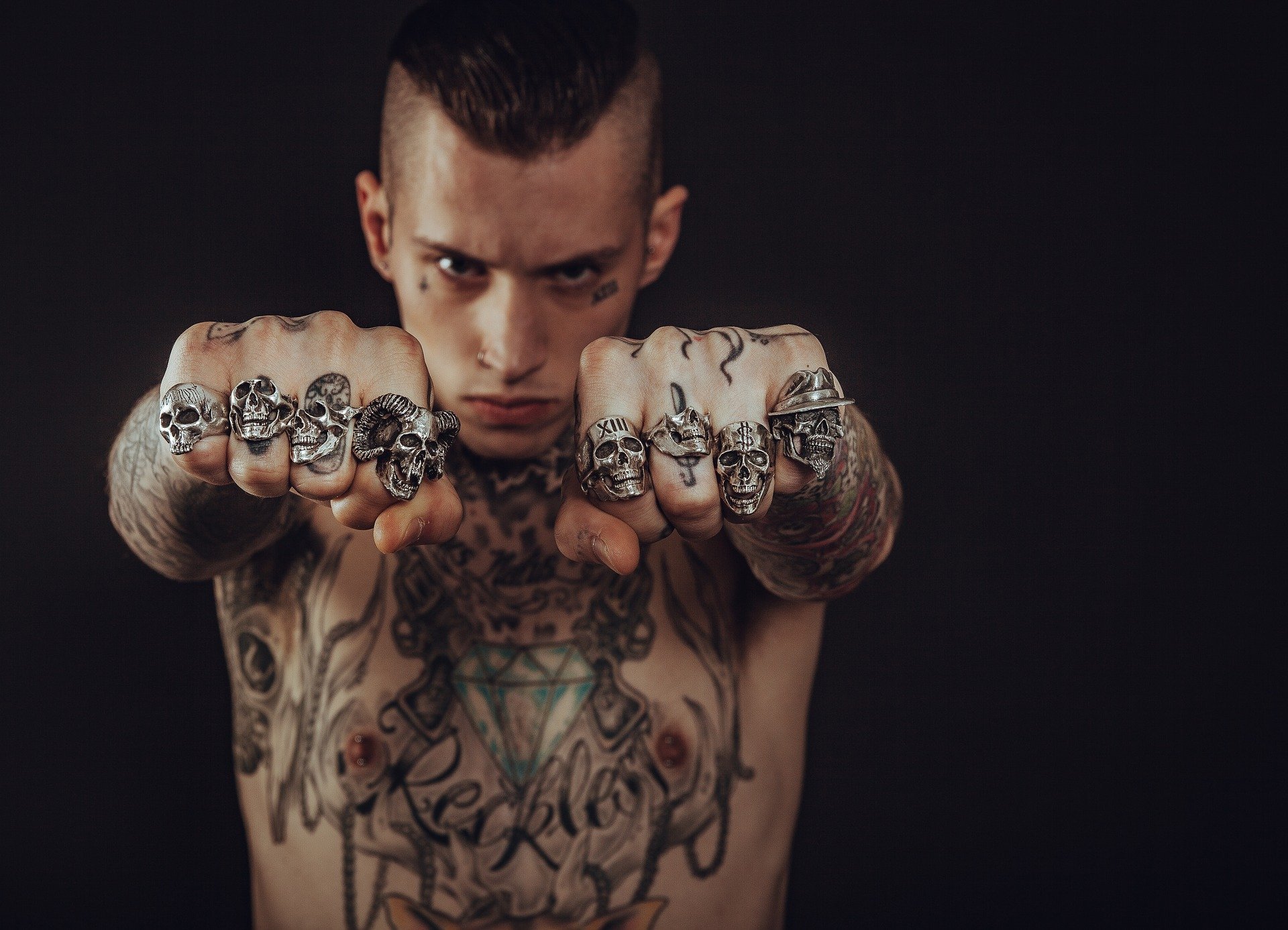 Foto de homem tatuado mostrando mãos com anéis