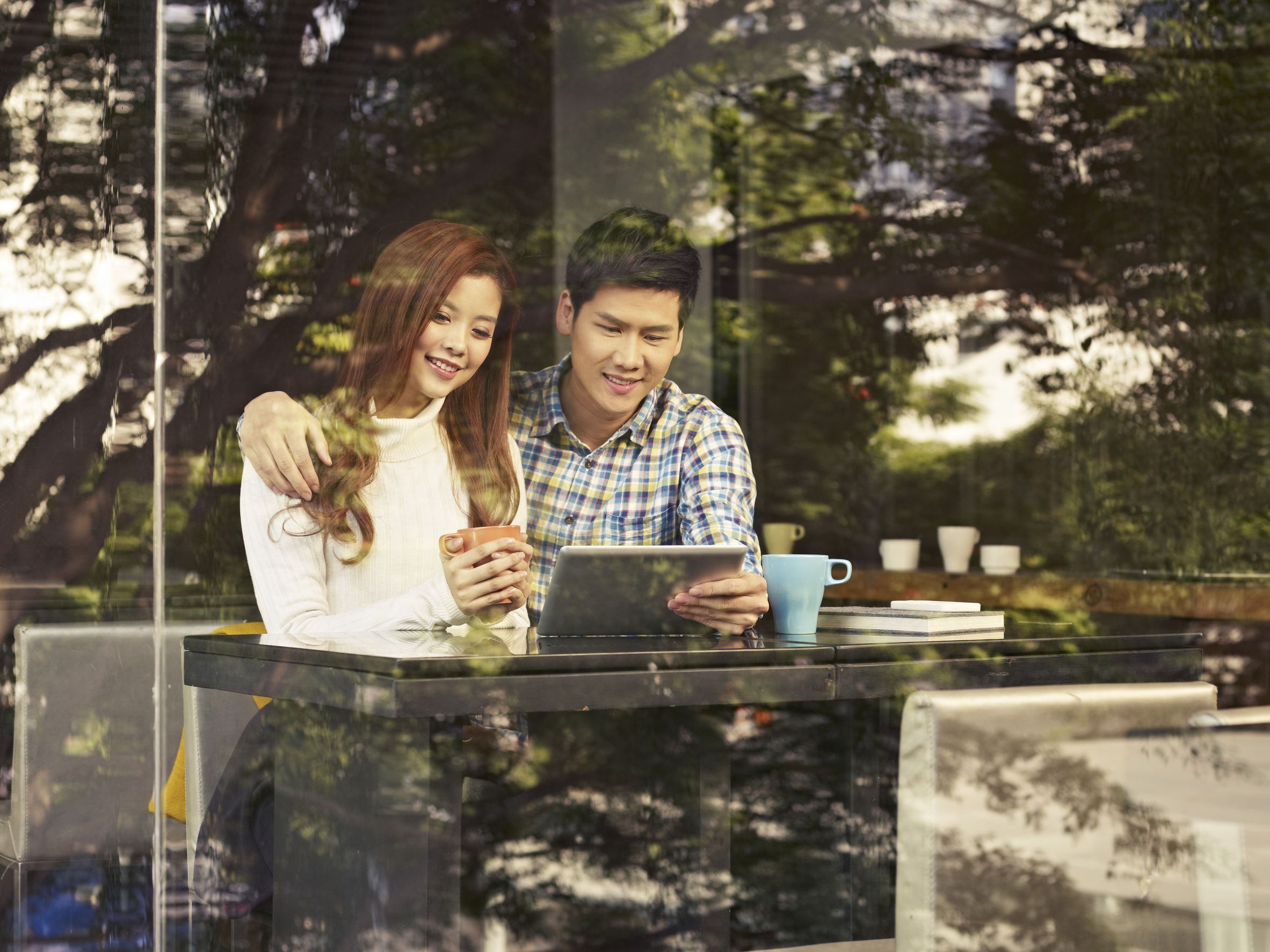Foto de casal sentados em mesa de restaurante, mexendo em tablet