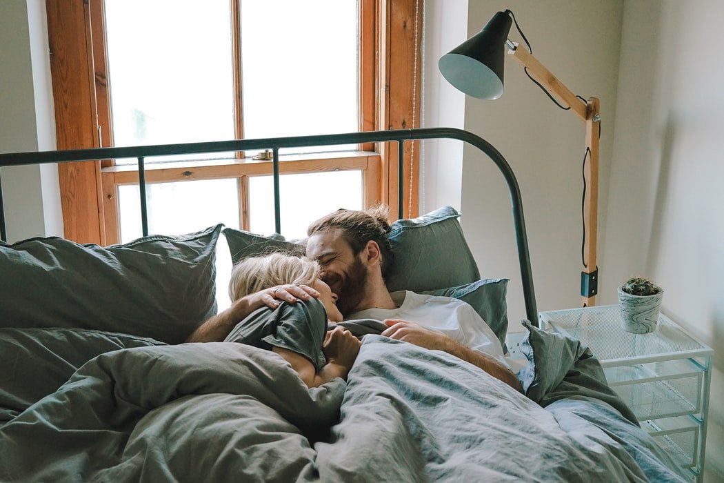 Homem e mulher deitados em uma cama, abraçados e sorrindo.