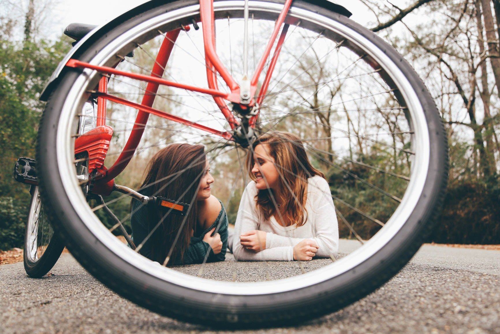 Duas meninas sorrindo uma para a outra atrás da roda de uma bicicleta.