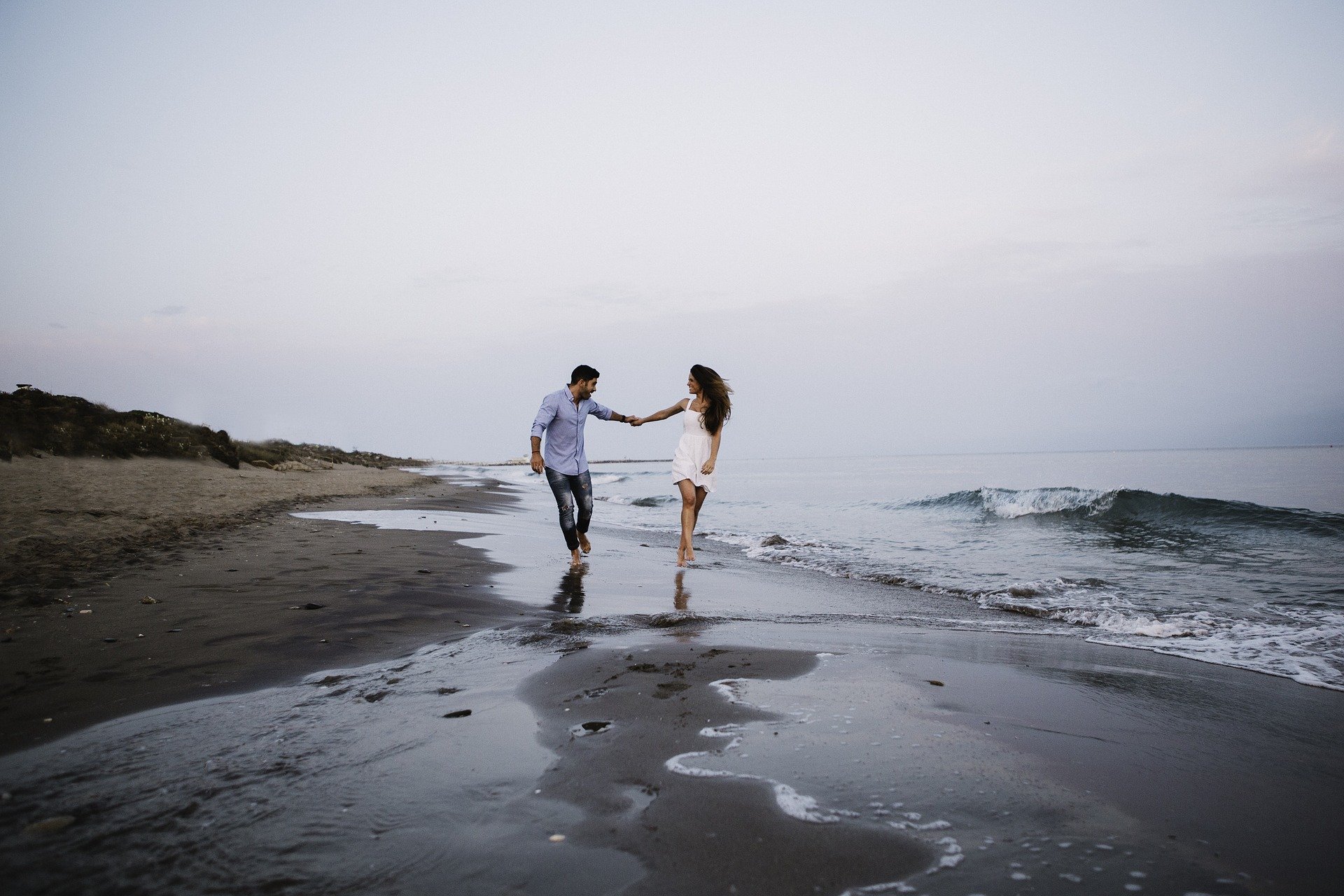Casal caminhando a beira mar, de mãos dadas