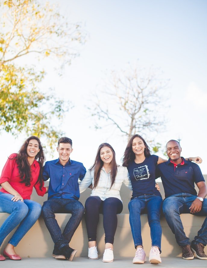 Grupo de amigos jovens sentados lado a lado e sorrindo.