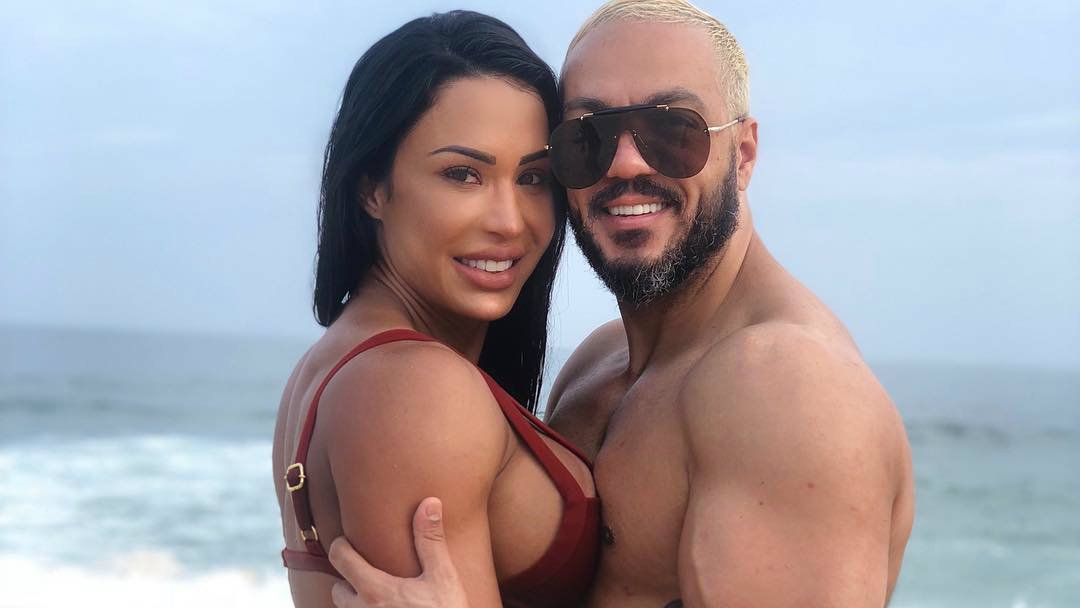 Gracyanne Barbosa e Belo sorrindo abraçados em frente ao mar