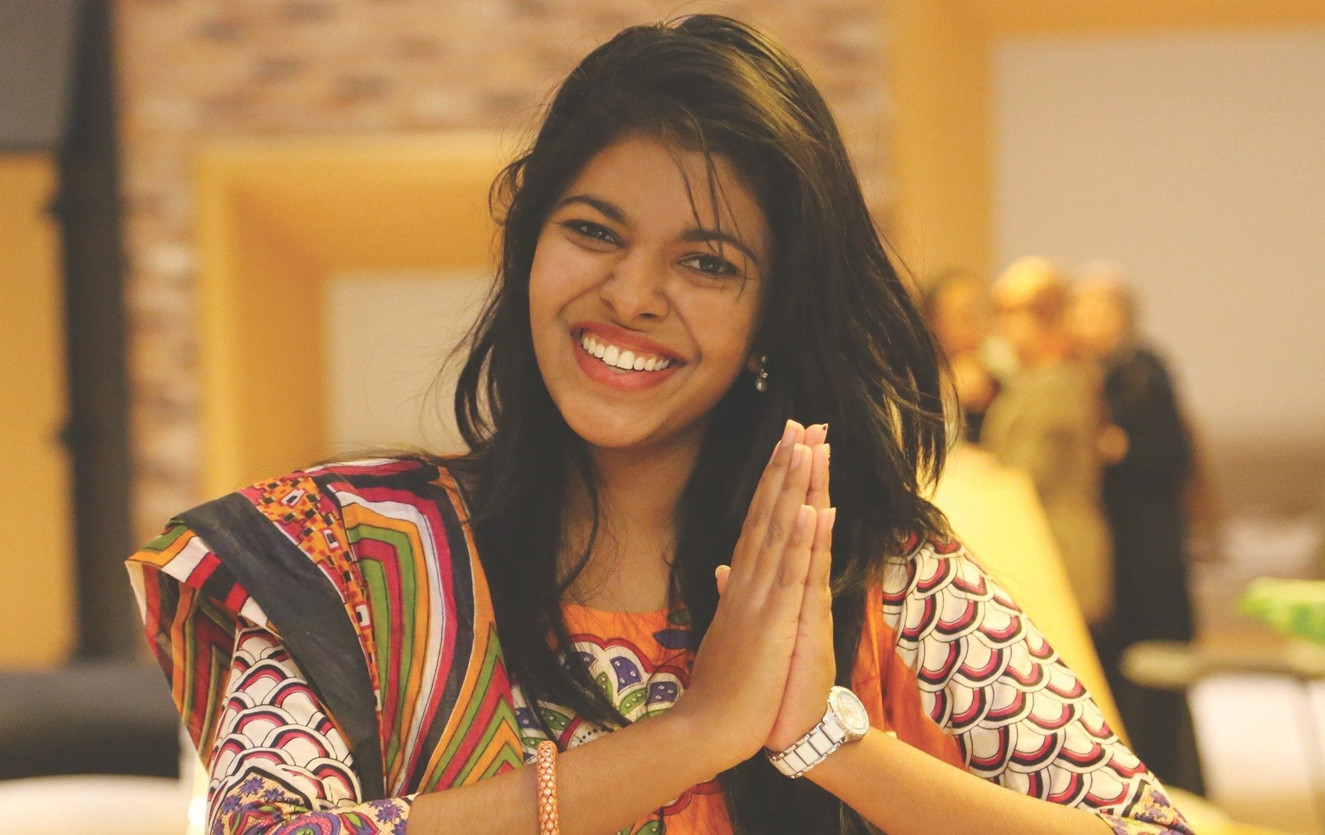 Foto de mulher morena, vestindo sari indiano, sorrindo com as mãos juntas