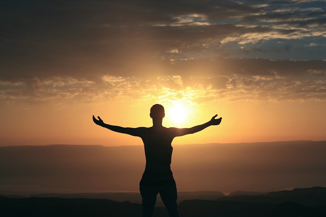Foto de pessoa com braços abertos assistindo pôr do sol