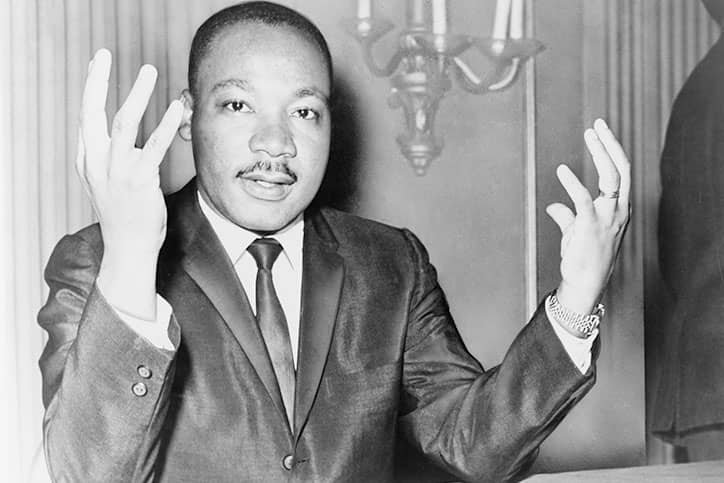Martin Luther King olhando para frente com as mãos para cima
