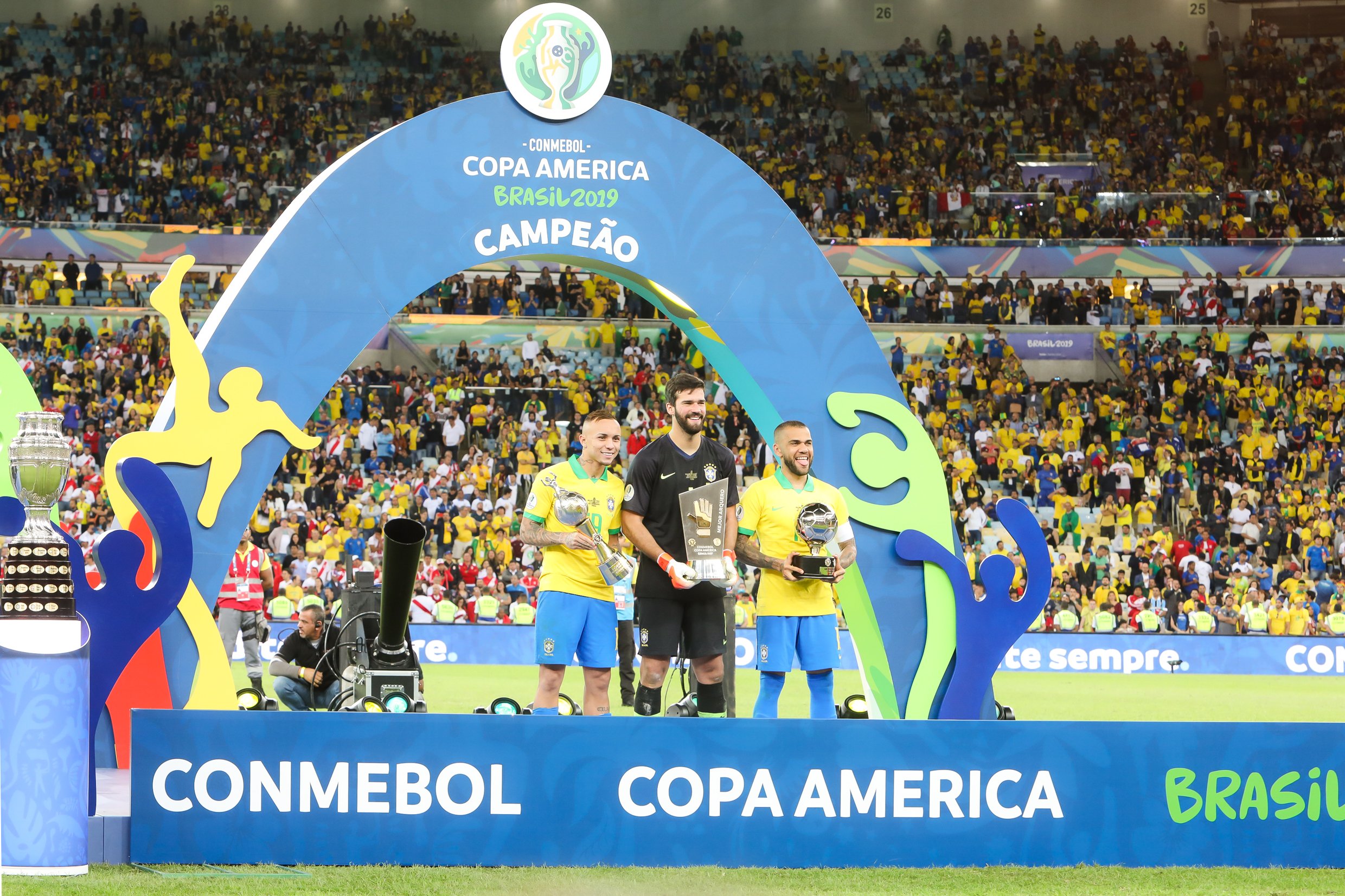 Estande da Copa América em estádio e jogadores segurando troféus