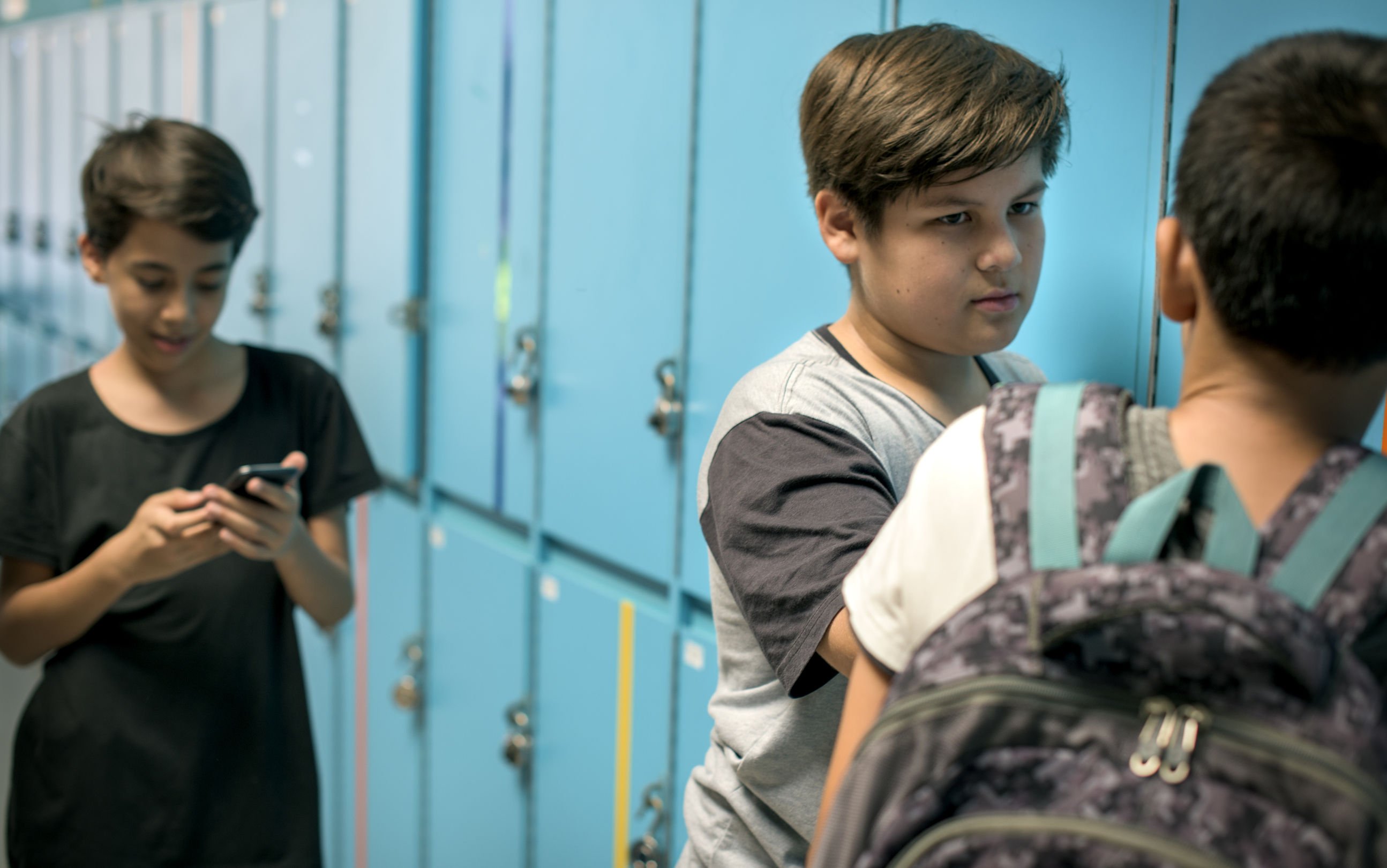 Meninos em corredor de escola, perto de armários azuis