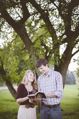 Casal lendo a Bíblia e sorrindo debaixo de árvore