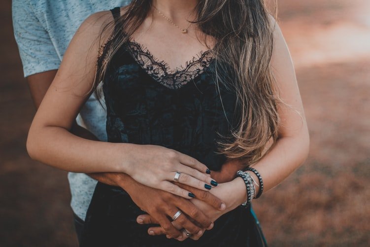 Homem abraçando mulher e ambos com as mãos entrelaçadas sobre seu ventre