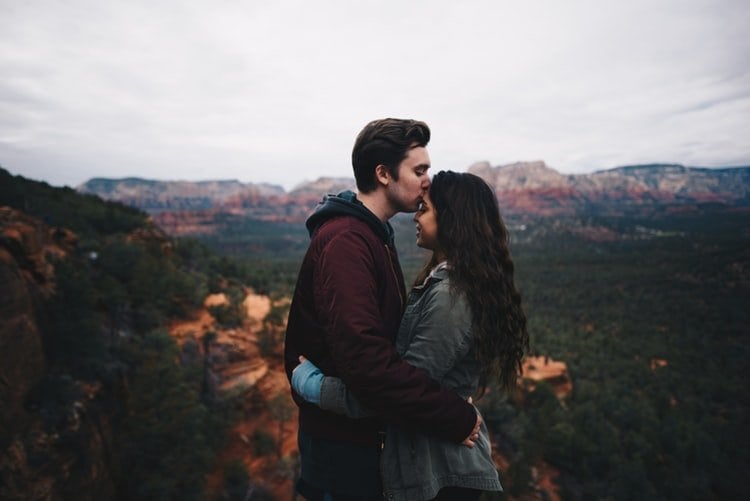 Homem beijando testa de mulher e montanhas ao fundo