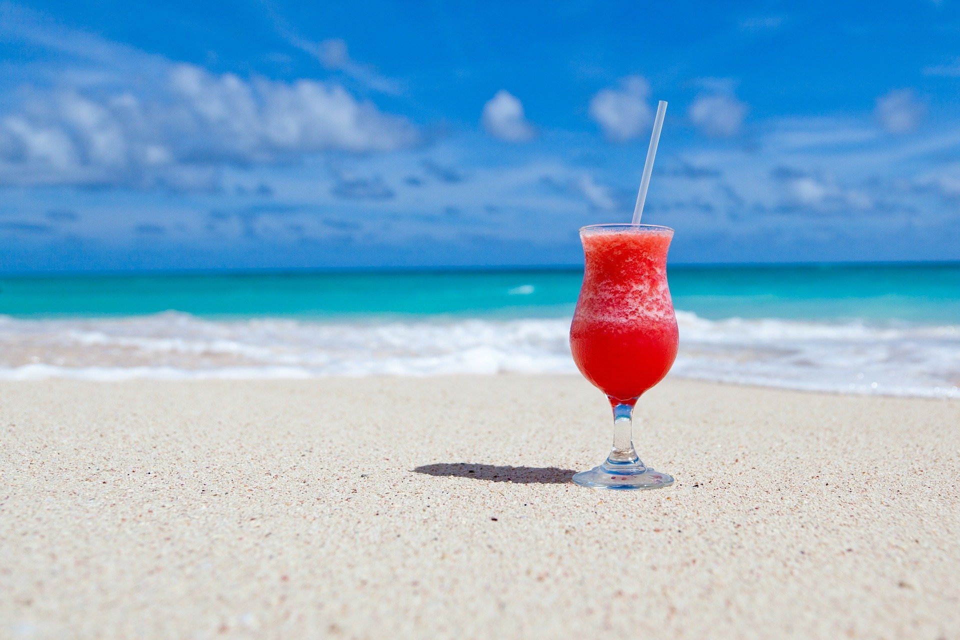 Foto de drink vermelho colocado na areia de praia perto do mar