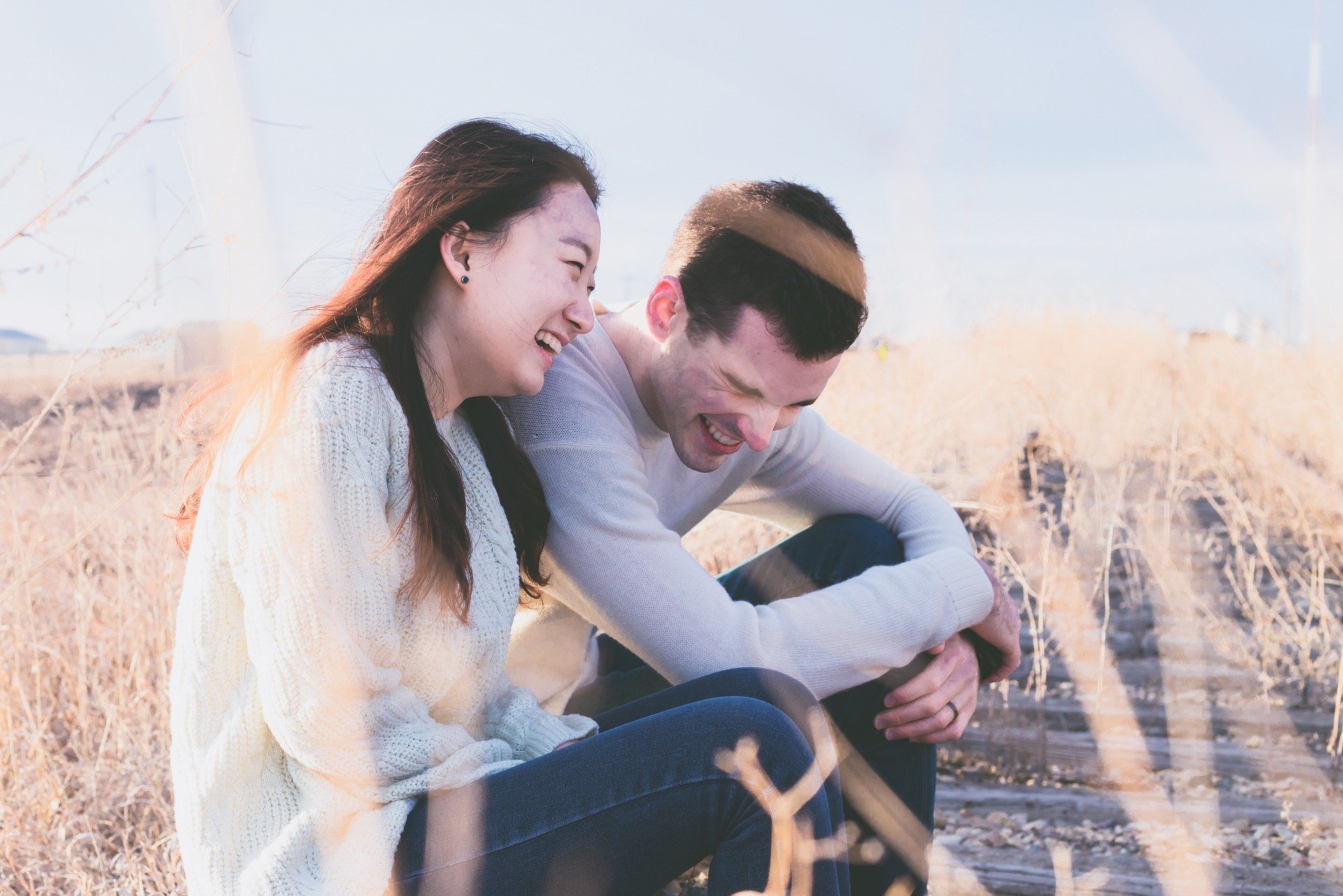 Foto de homem e mulher rindo, sentados em campo de trigo
