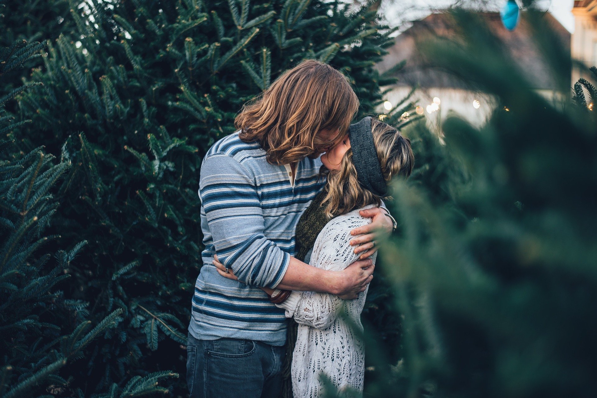 Homem beijando mulher perto de árvores de natal