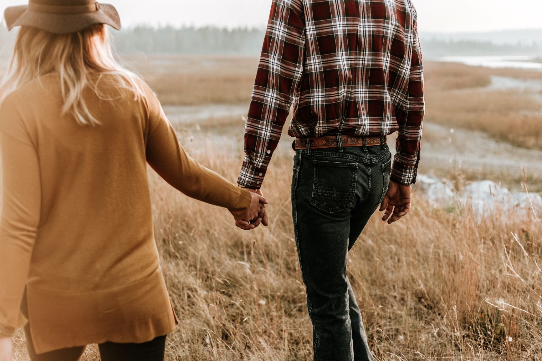 Homem e mulher de mãos dadas caminhando pelo campo.