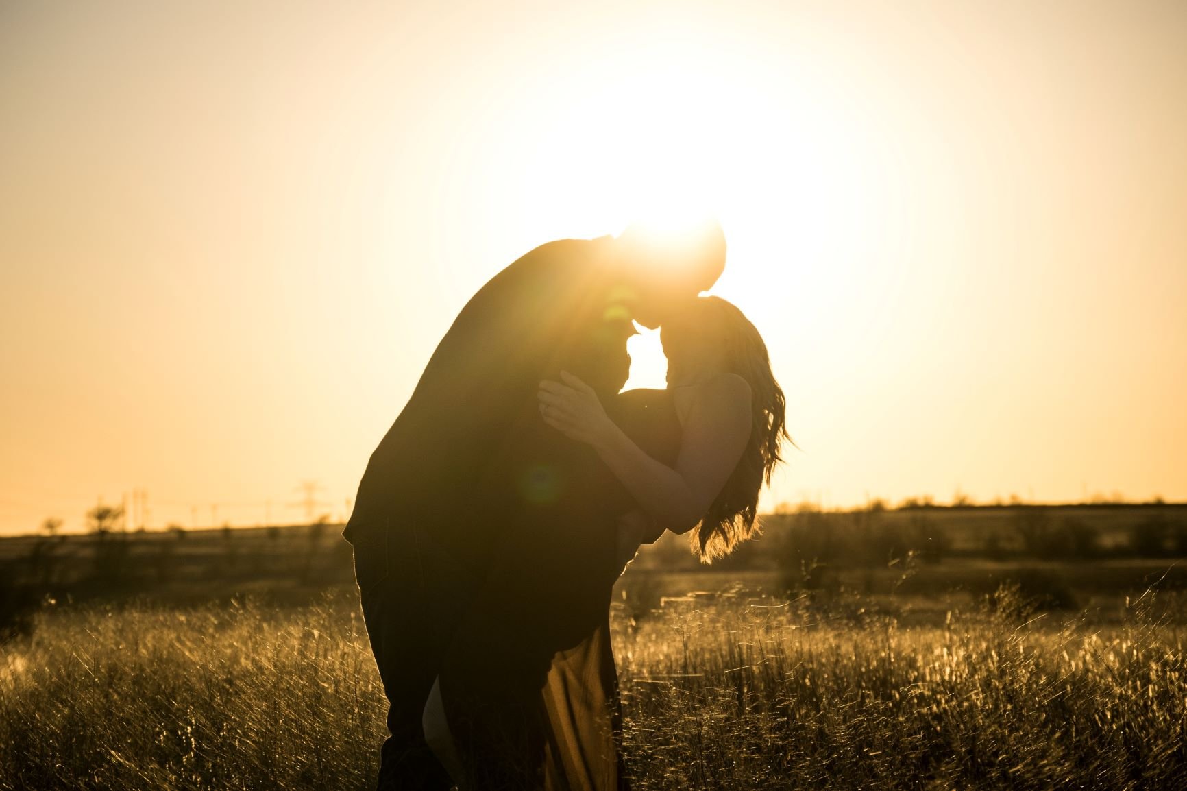 Casal se beijando no campo, sob o pôr do sol.