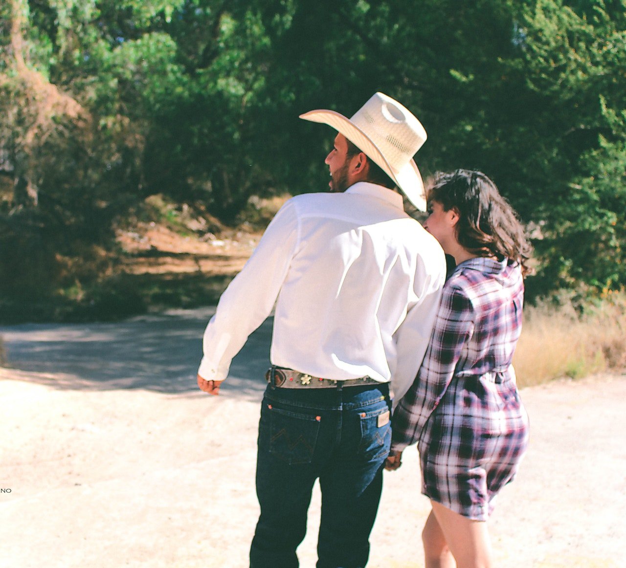 Homem e mulher de costas, no campo, usando blusa xadrez e chapéu de cowboy.