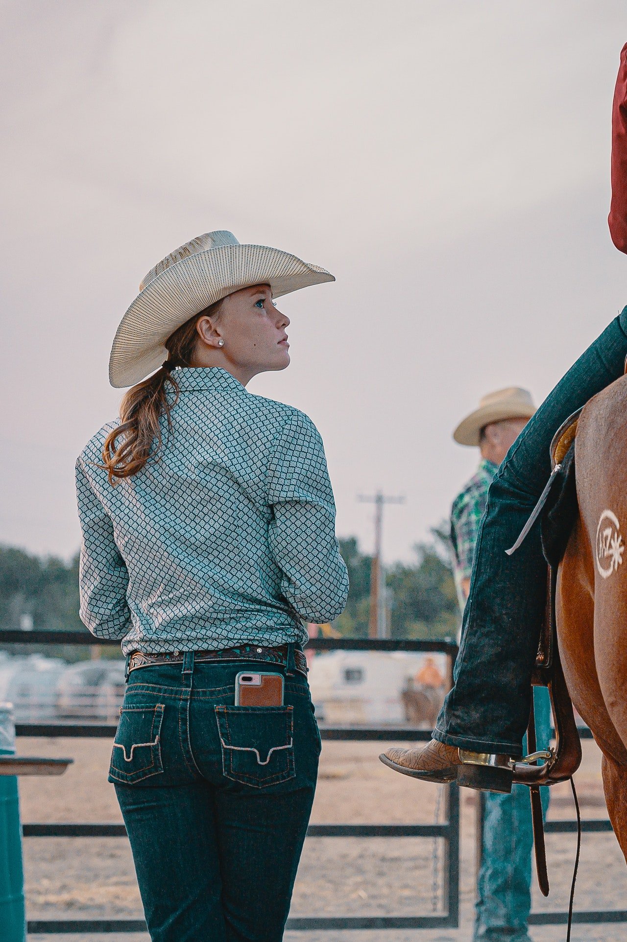 Mulher usando jeans e chapéu olhando para um homem montado em um cavalo.