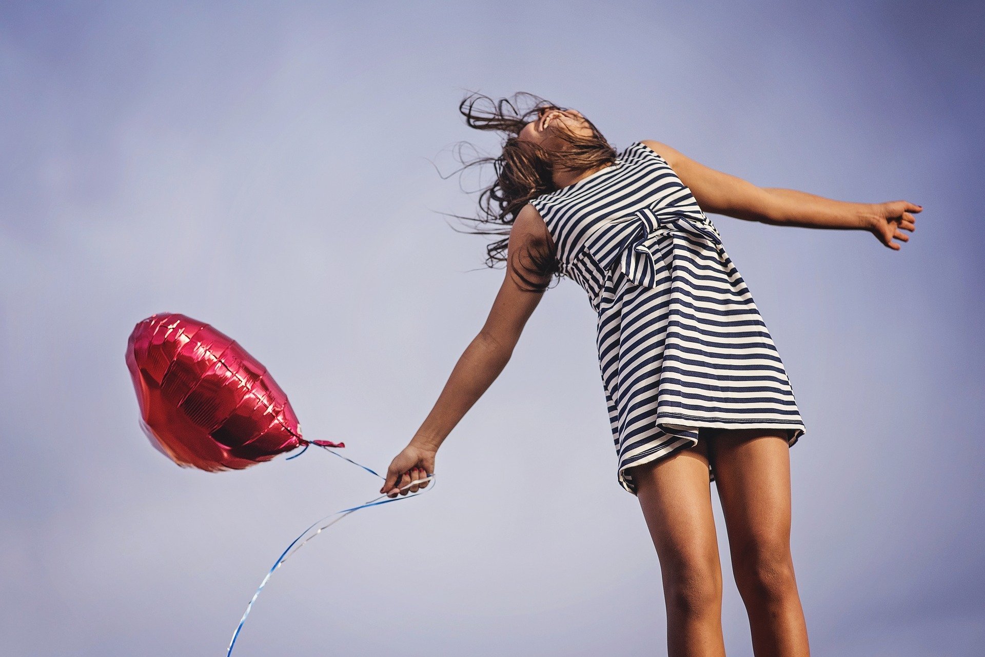 Foto de menina com braços abertos segurando balão em formato de coração