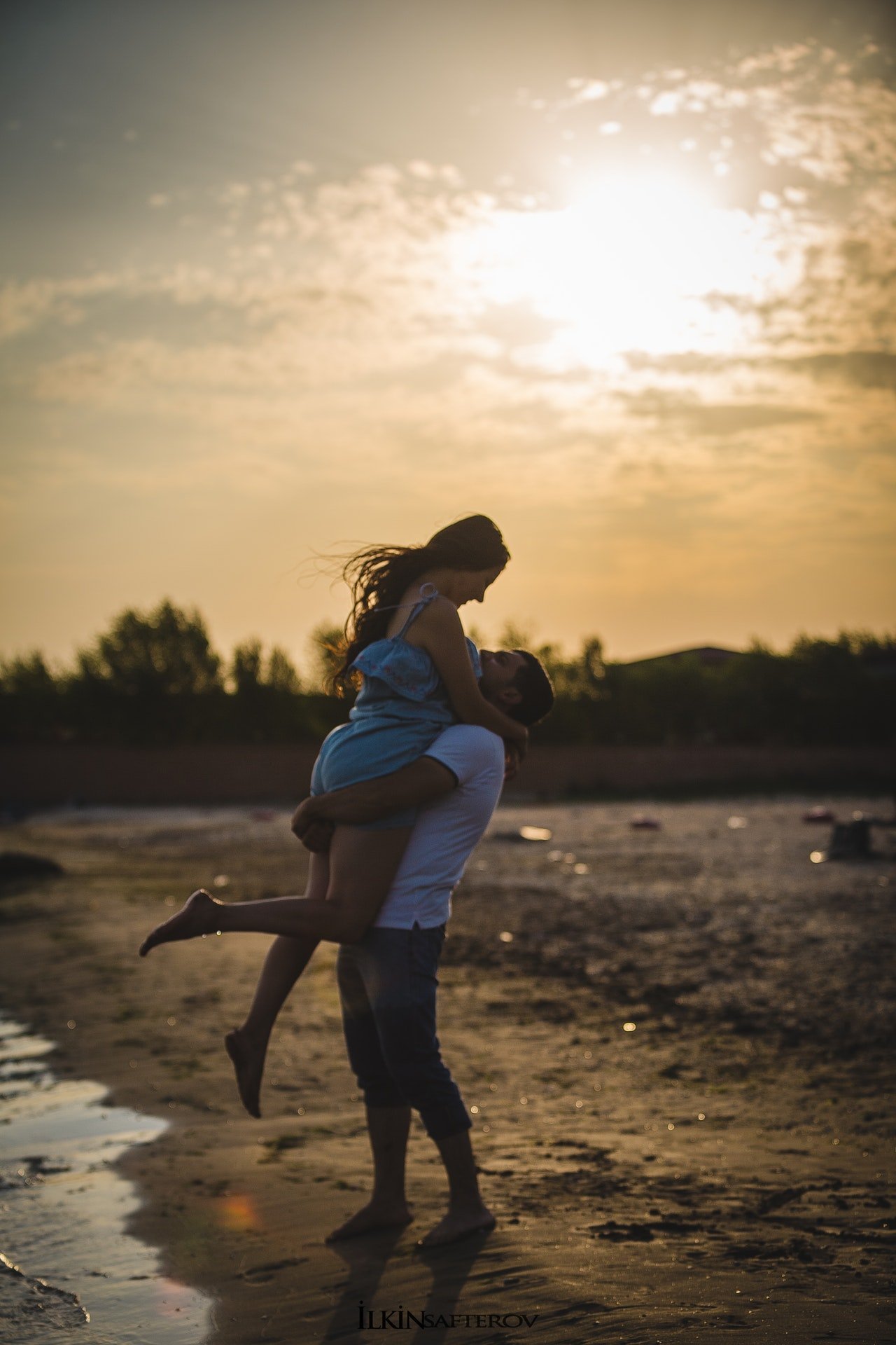 Homem levantando mulher em seus braços, na praia, em frente ao mar.